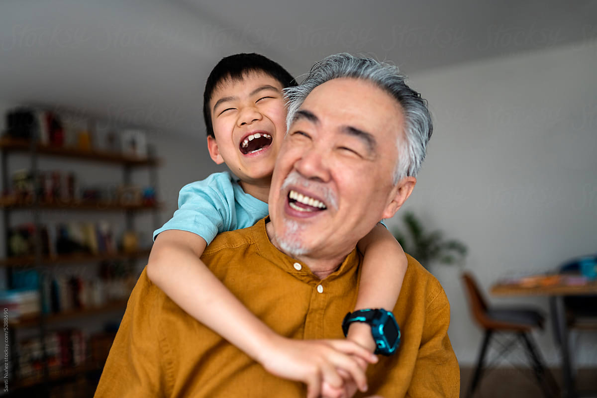 Grandson embraces laughing grandfather in cozy home.
