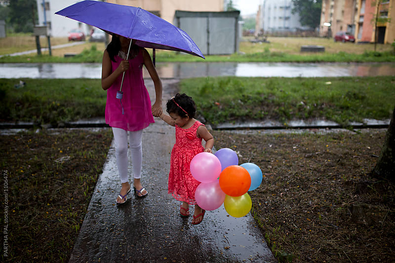 Little girl with elder sister walking together with umbrella with balloon in hand of the kid