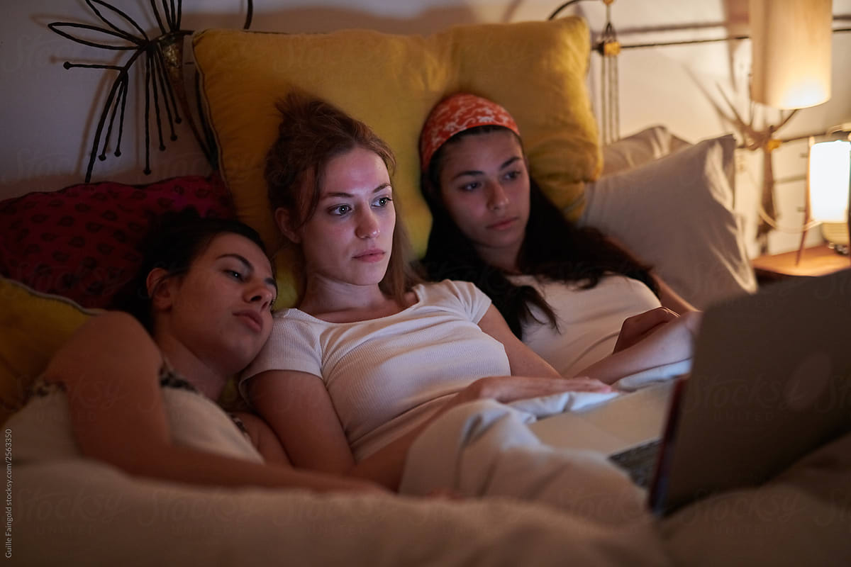 Girls in bed watching movies on laptop.
