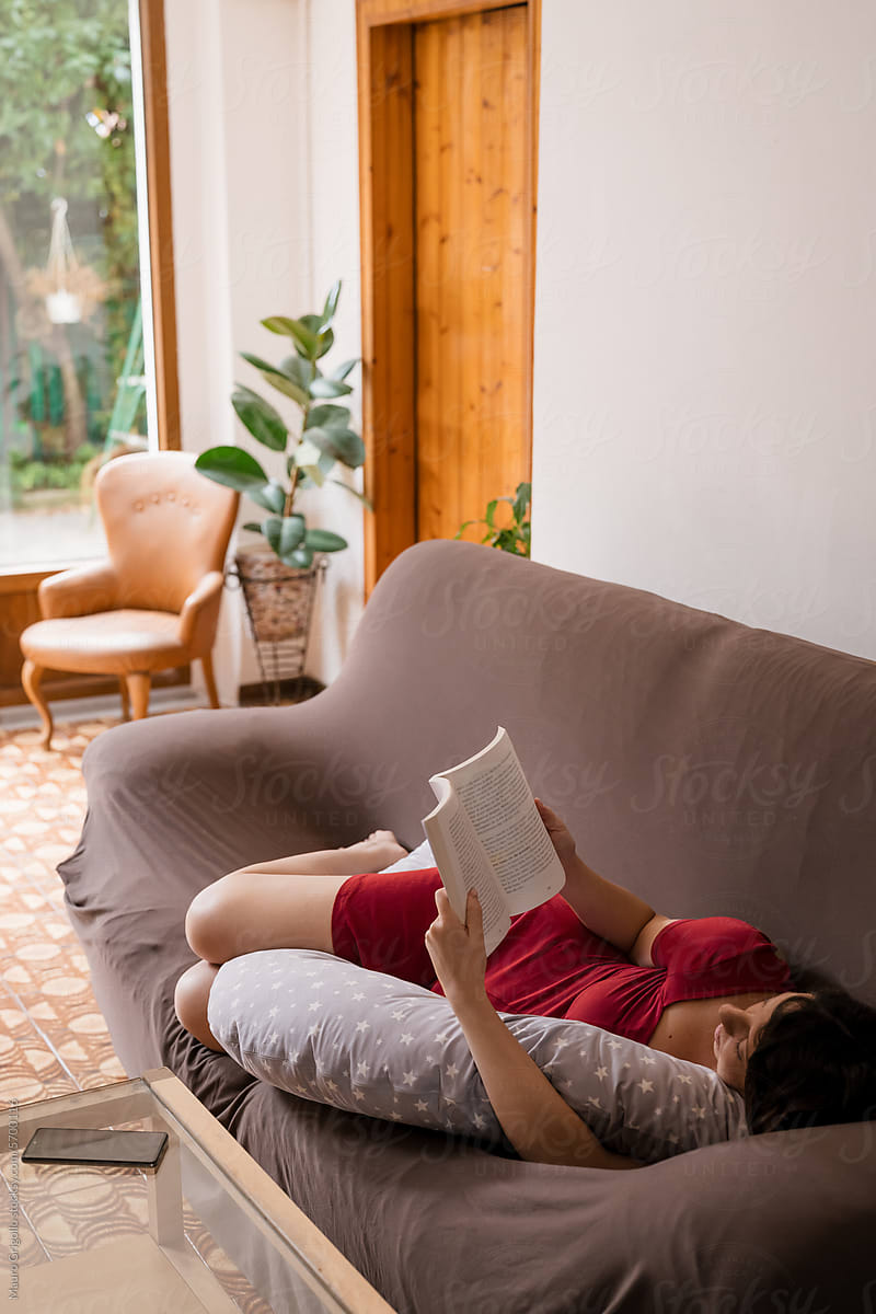 A woman reading a book while lying on the sofa