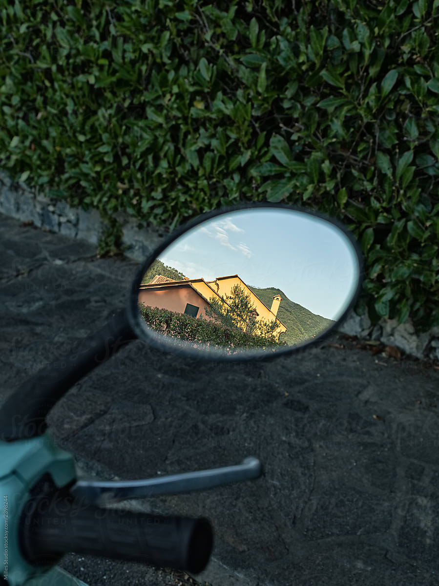 Reflection of house in small mirror of motorbike