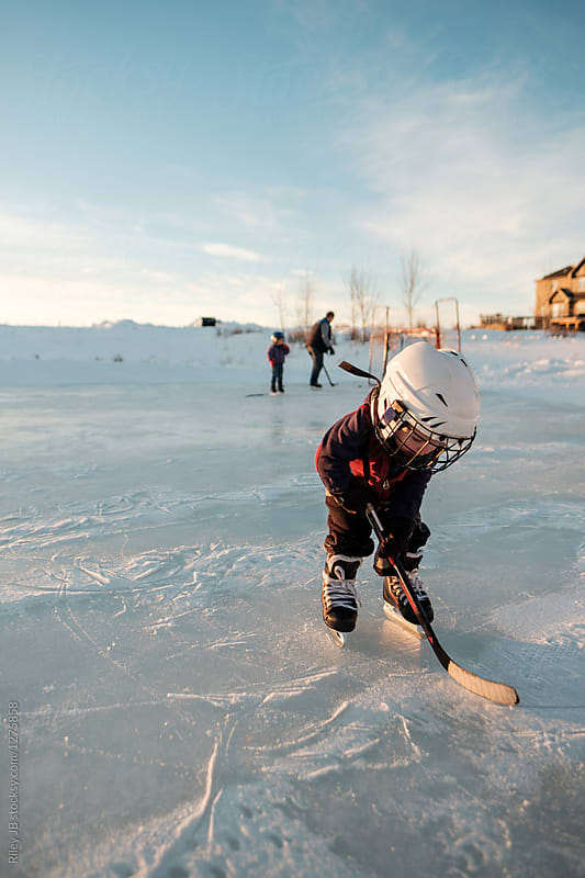 A little toddler skates on a frozen pond with a hockey stick