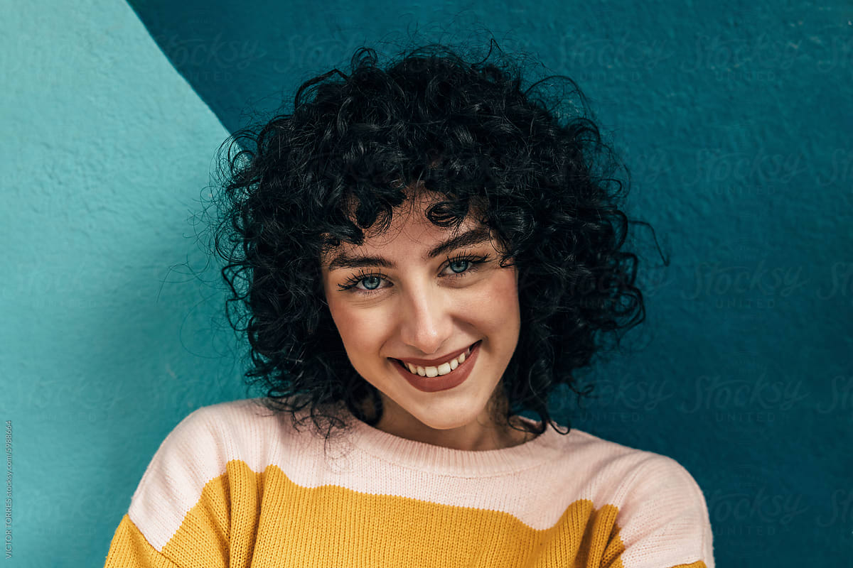 Smiling young woman with curly hair on a blue background