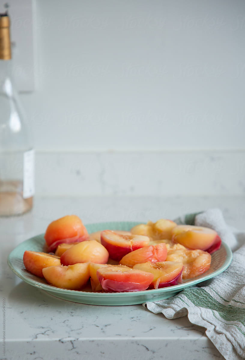 Peaches that have been poached in a wine syrup cooling on a plate.