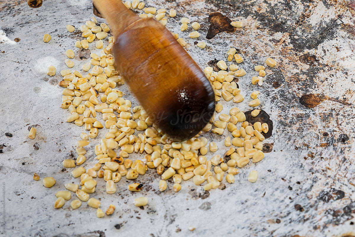Kernels of corn on a comal moved by a wooden spoon