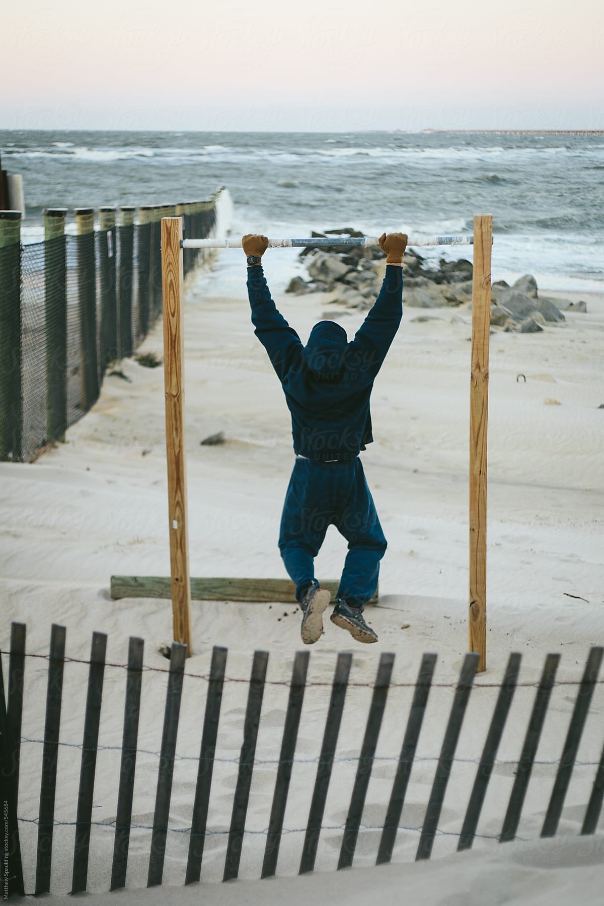 Man in sweat shirt doing pullup exercises on beach outdoors