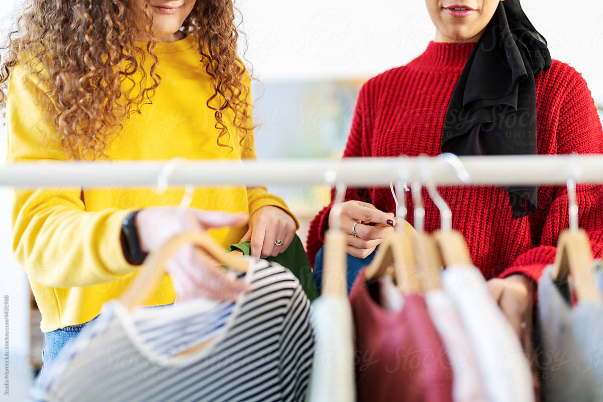 Diverse women hanging clothes on rack in new flat