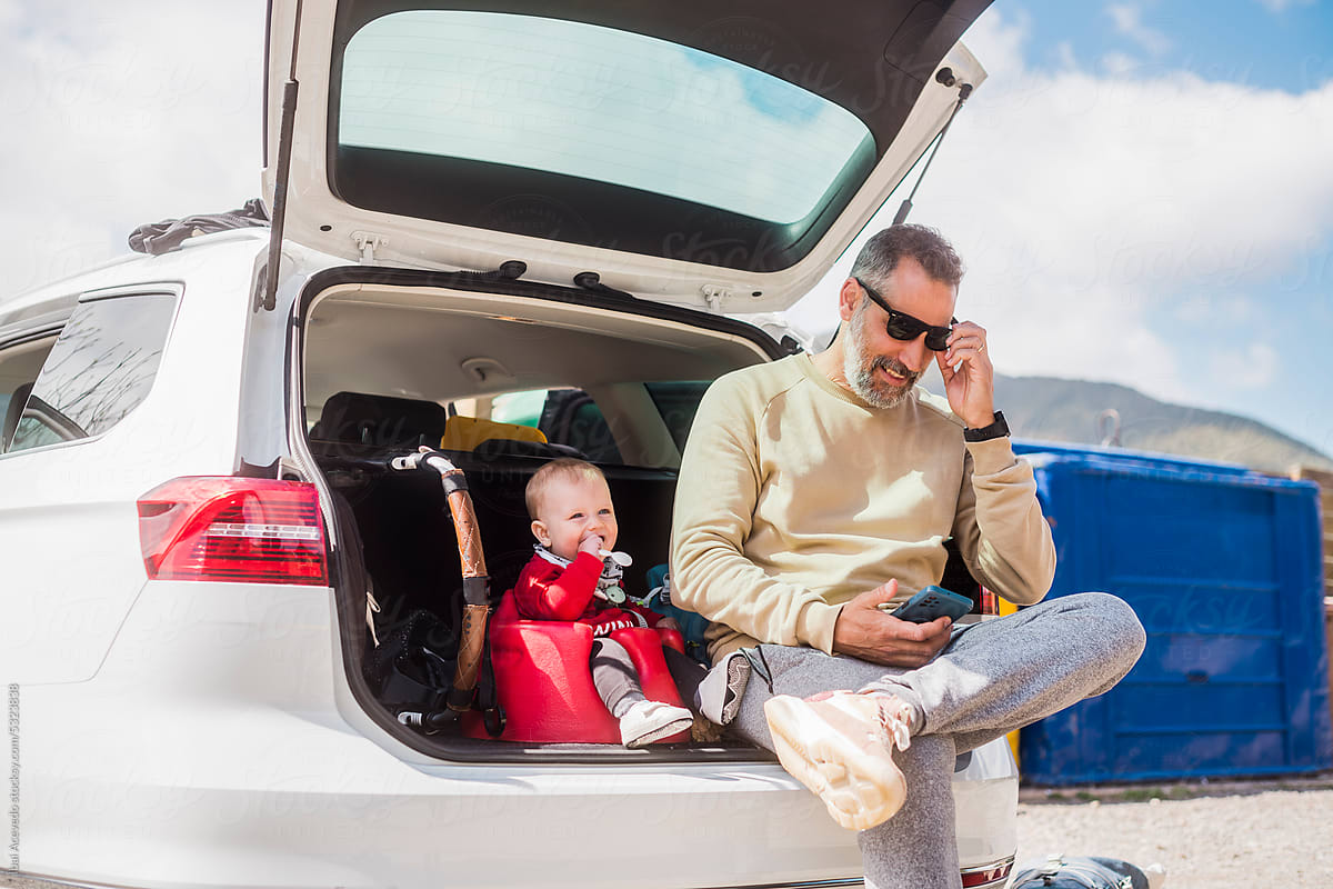 Father and newborn sitting at car trunk