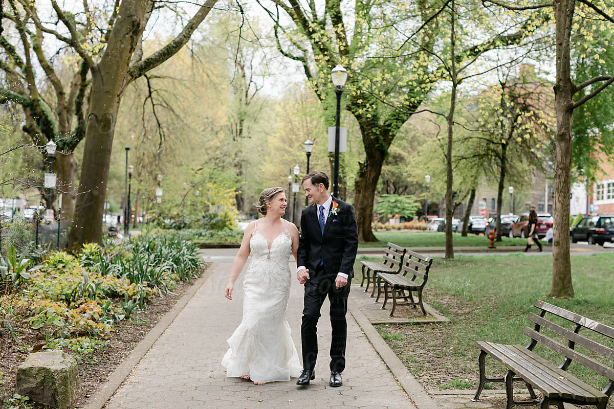 A Smiling Bride and Groom Walk through a City Park Together