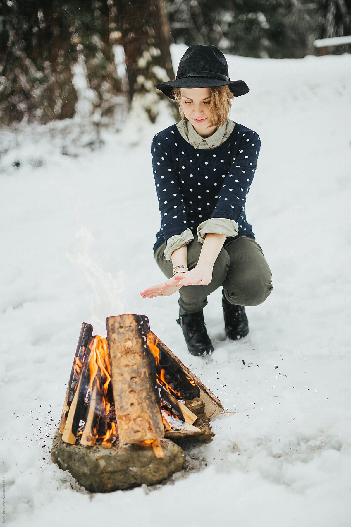 Young fashionable women sitting warming hands by fire in the snow