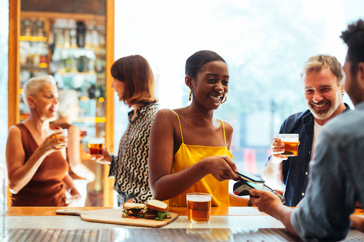 Cheerful black woman paying for drink in bar