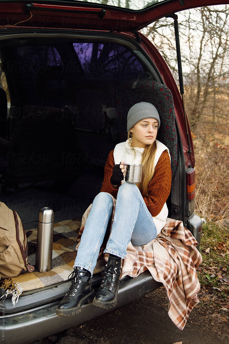 Woman with hot beverage sitting in car trunk