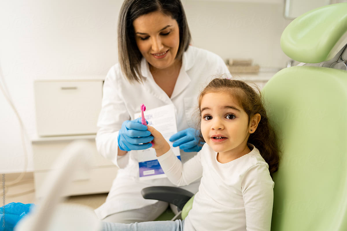 Dentist showing little girl how to proper brush her teeth