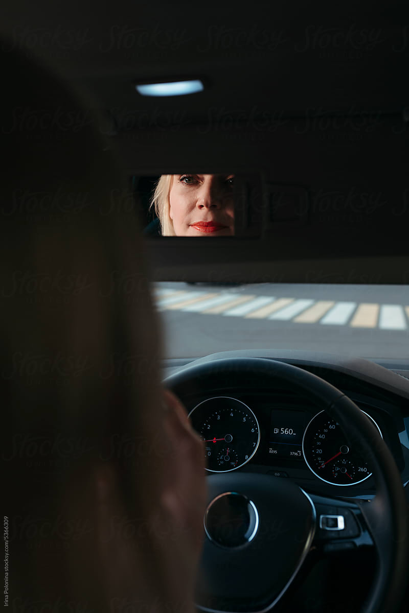 Middle-aged woman does makeup while sitting in car.