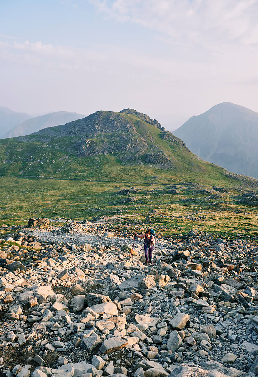Female walker at sunrise climbing up to Scafell Pike with Lingmell and Great Gable behind.