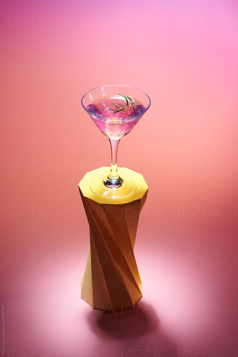Cocktail in vintage champagne glass with rosemary on geometric podium