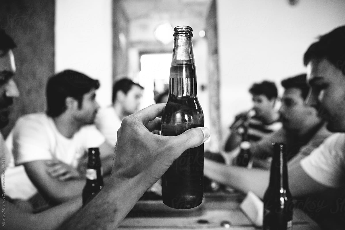 Man hand holding up a full beer bottle in front of a group of people sitting at a table
