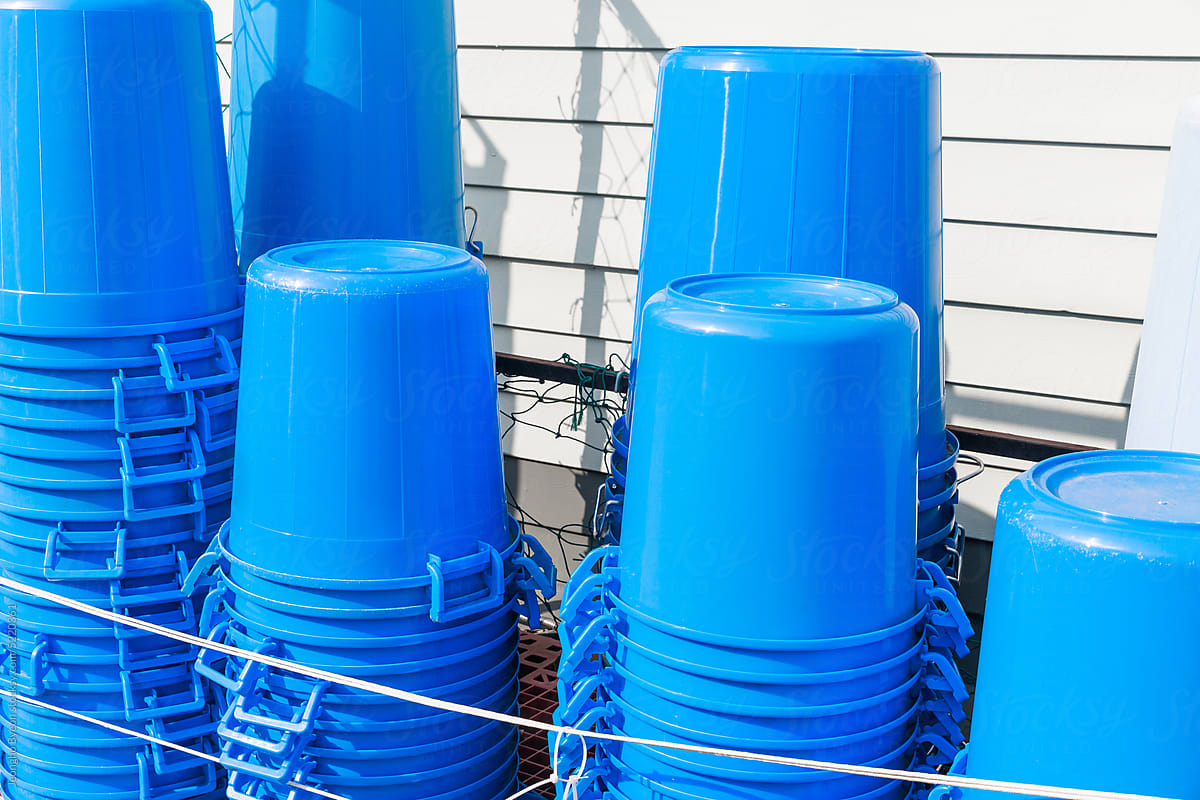 Blue plastic buckets stacked next to a white wall.