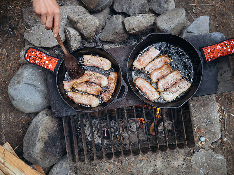 Bacon sizzling in cast iron skillets over campfire in National Park