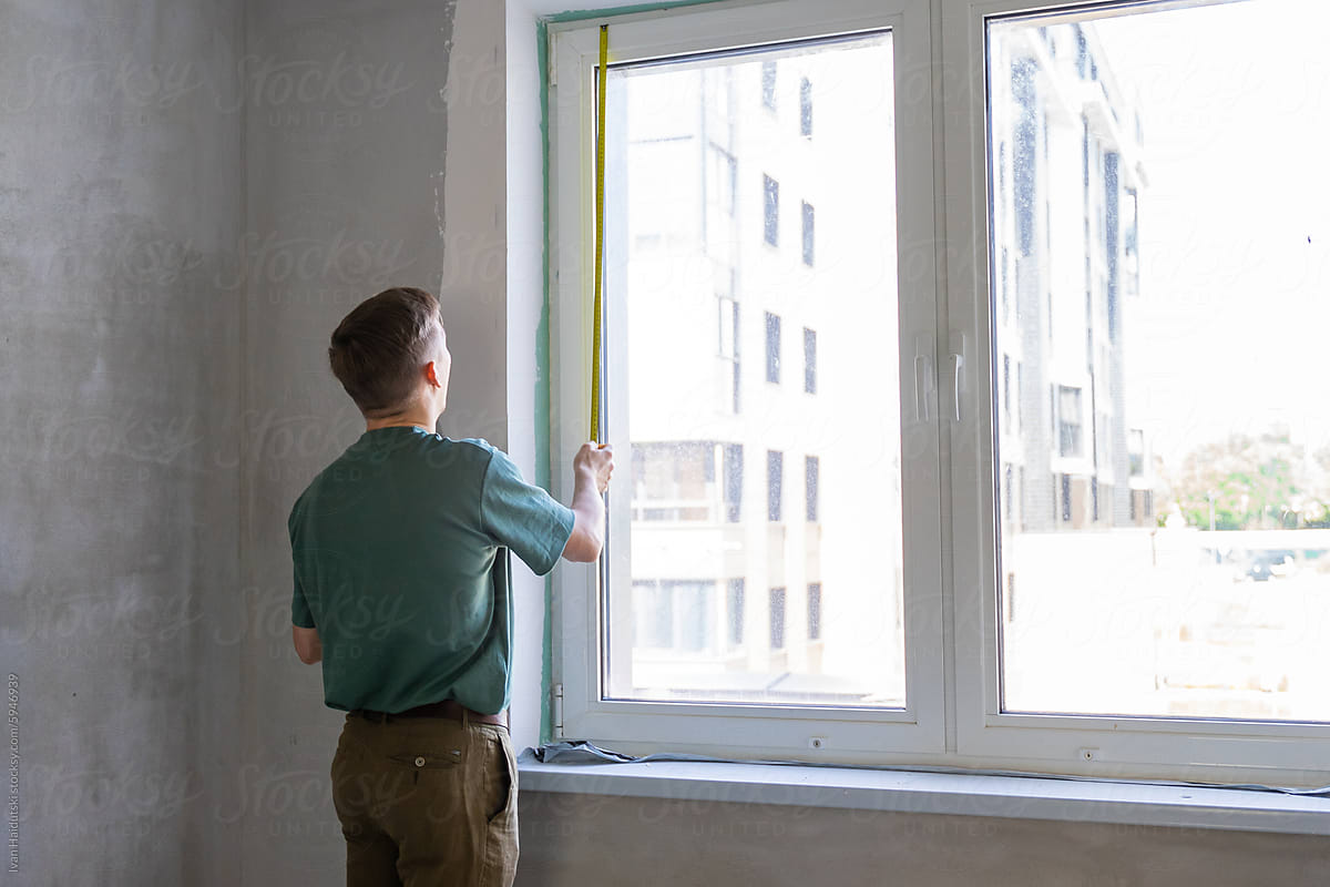 man measuring the size of a window in a new home using measure tape