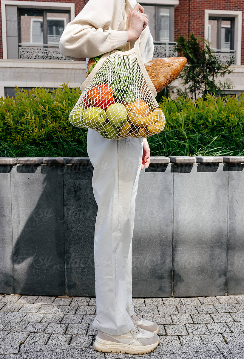 Crop woman with mesh bag of fruit, vegetables and bread