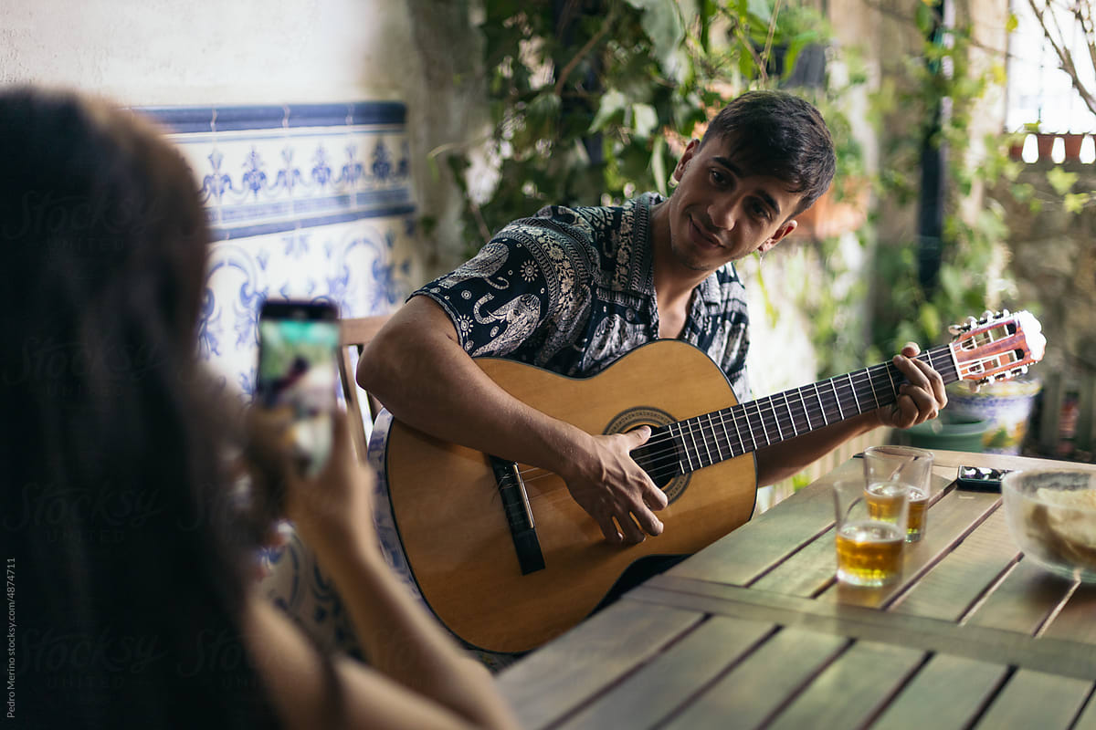 Man playing the Spanish guitar outdoors while his friend records him