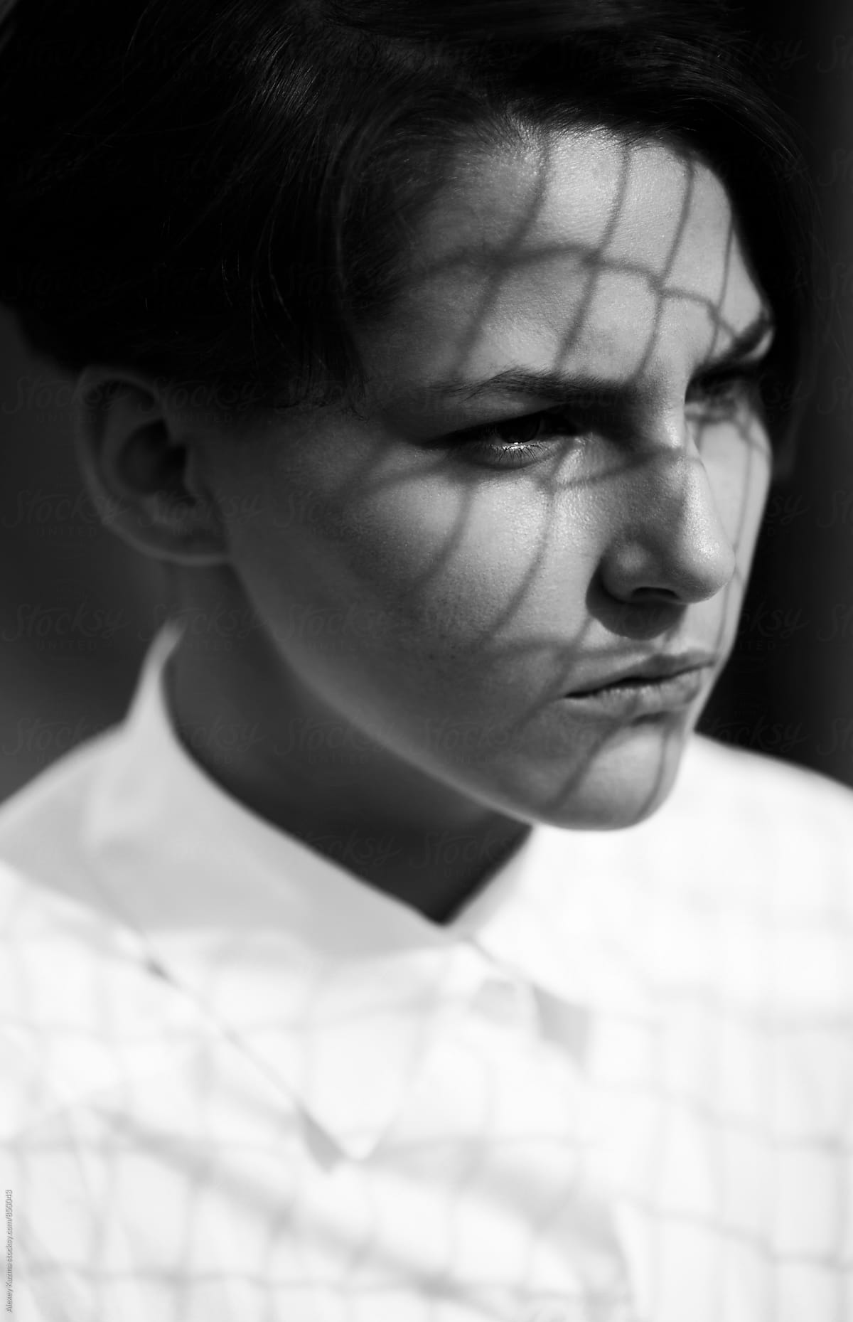 Portrait of androgyne with a geometric patterned shadow on her face .