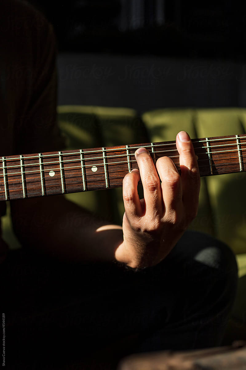 Close up of a male hand on the frets of a guitar in a dark background