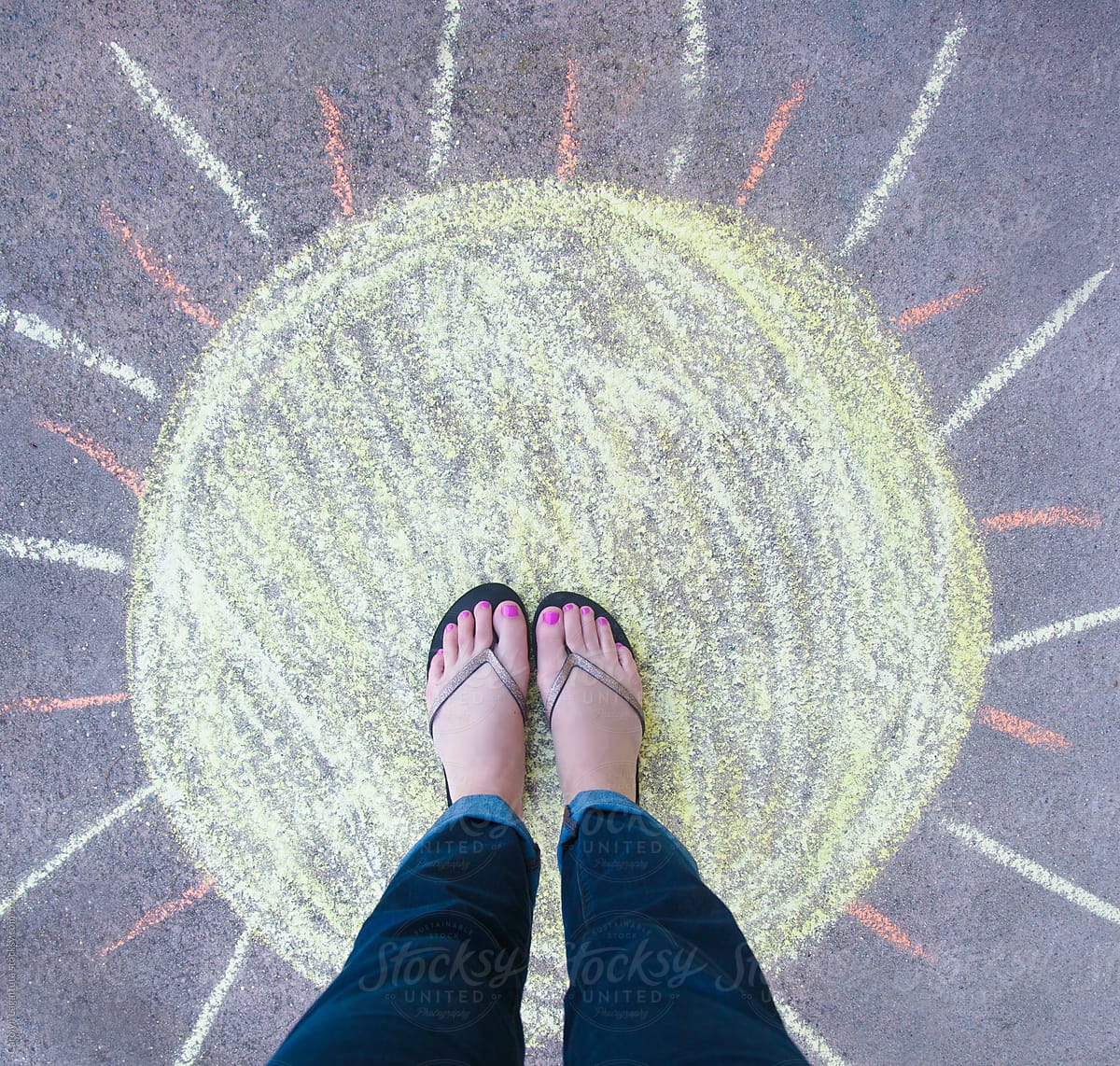 Feet in flip flops standing on a chalk drawn sun