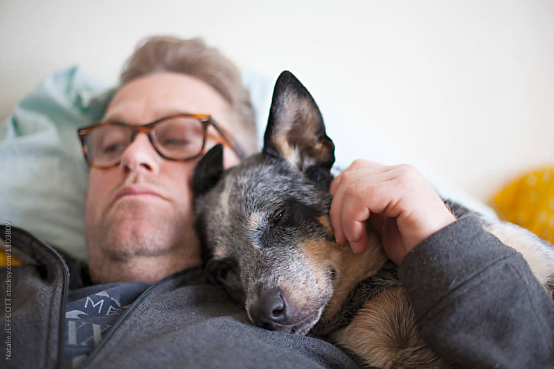 Middle aged man on his bed with his blue heeler dog