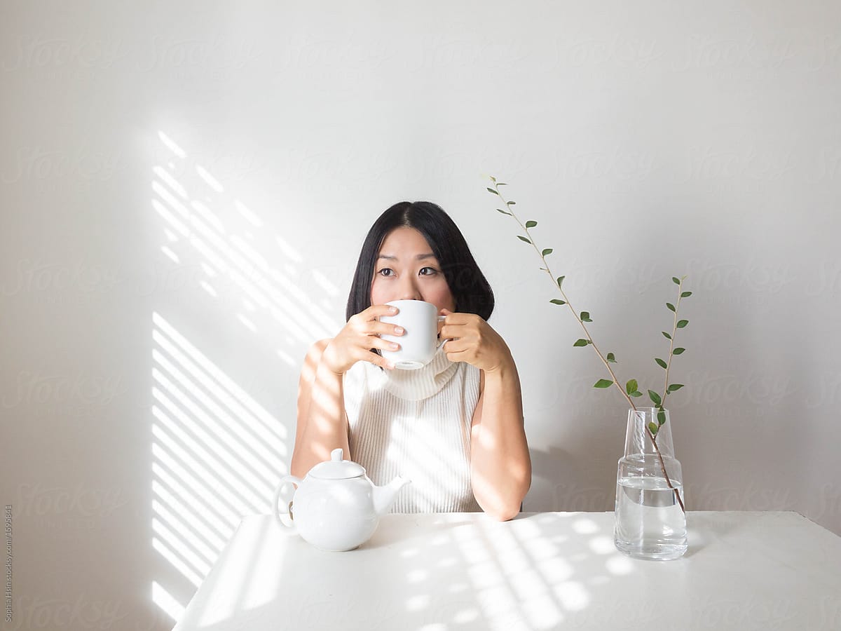 Portrait of young woman sipping tea at table with natural light