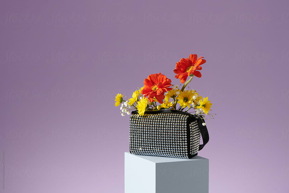 Sparkly handbag is full of colorful gerbera flowers on pastel