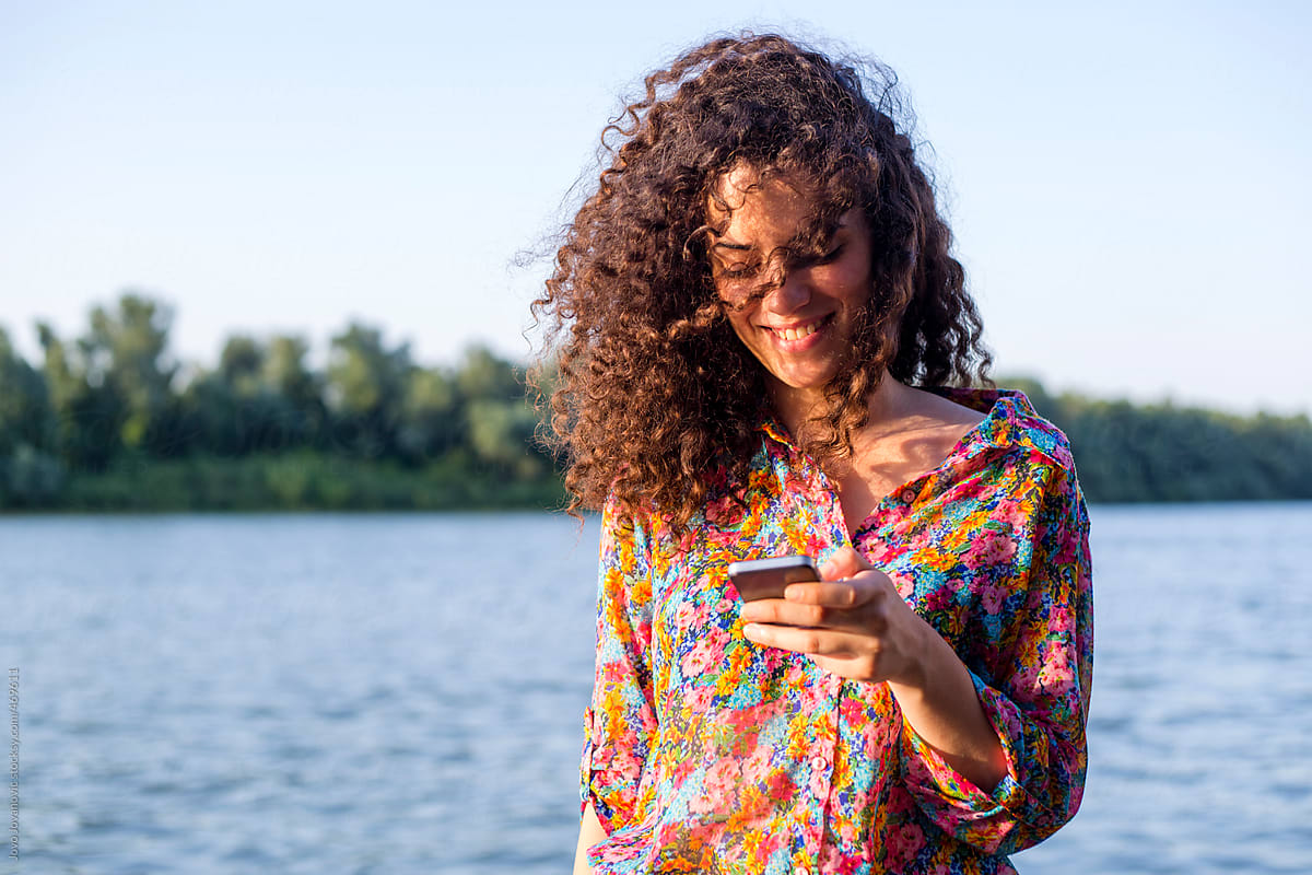 Girl with curly hair using her phone by the river