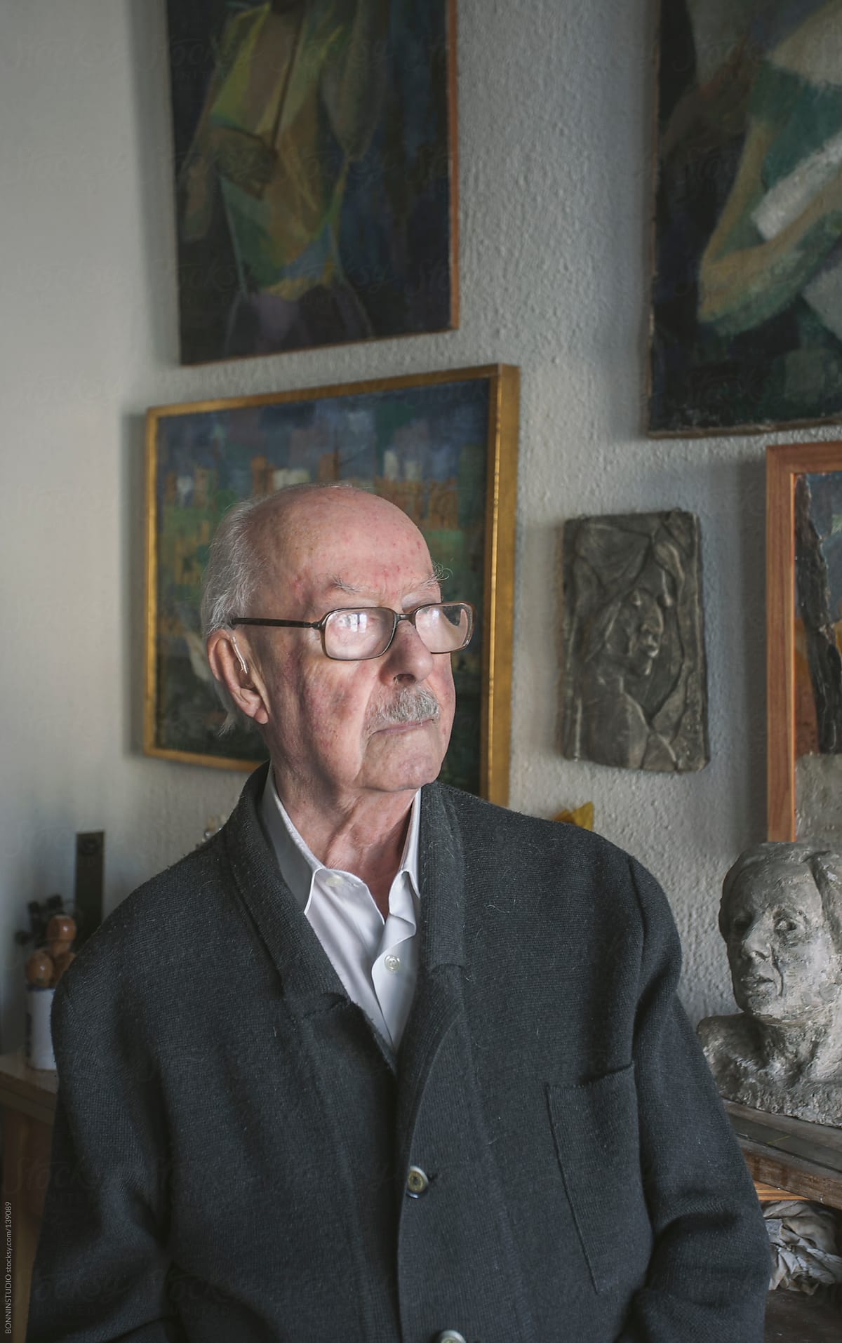 Portrait of old man standing on his studio of painting and sculpture.