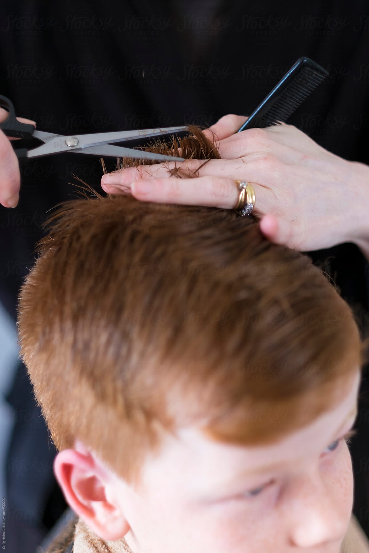 A boy having his hair cut with clippers and scissors.