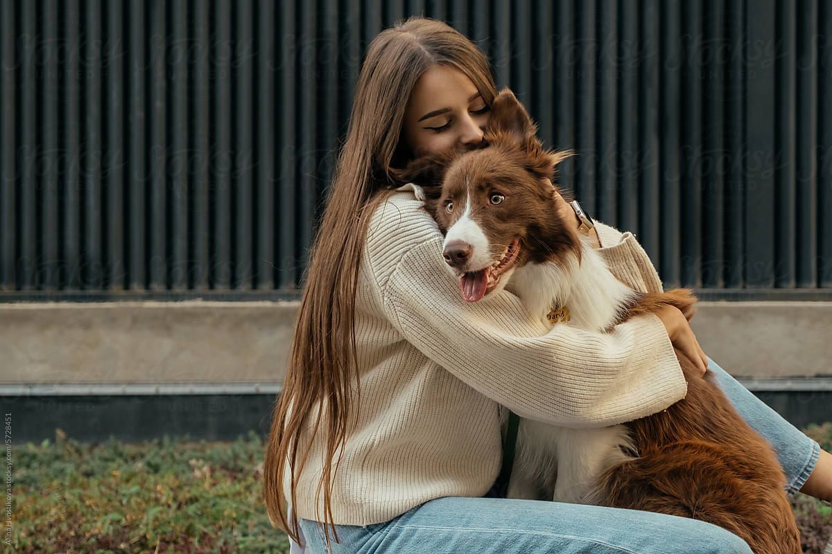 Happy woman caressing Border Collie dog while sitting on street in day