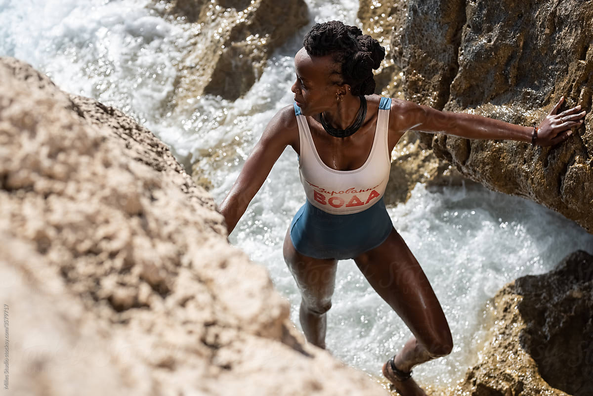 Black woman climbing on rocks and looking at sea
