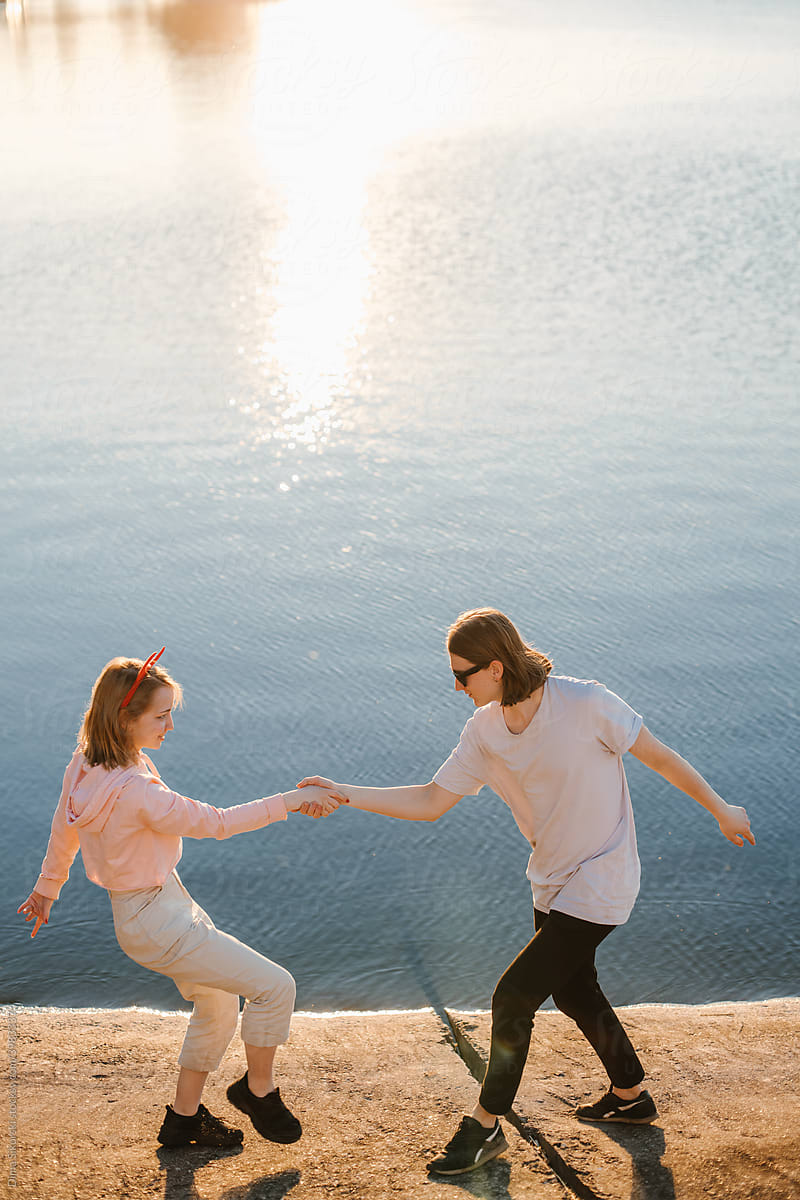 a young couple dances by the water at sunset