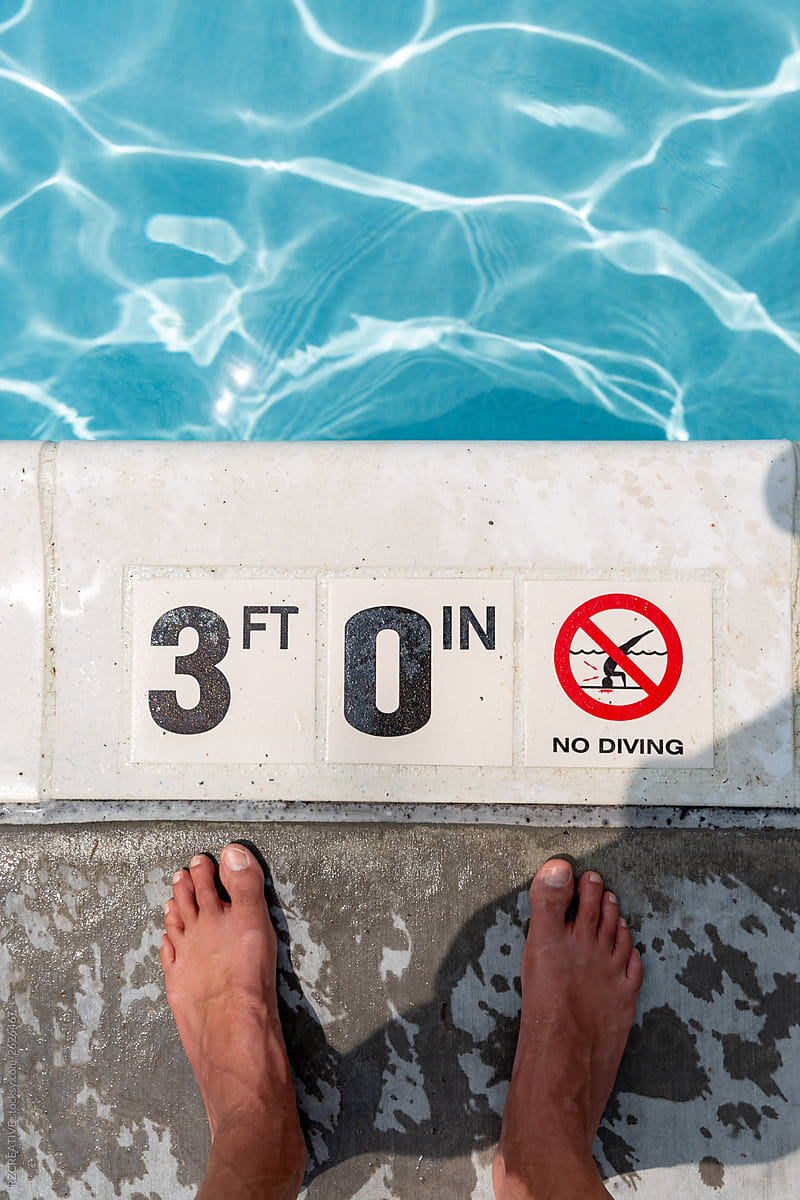 Feet in front of pool depth sign.