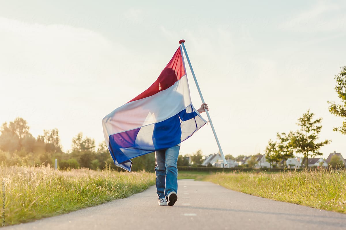 Boy walking a long road holding a Dutch flag  in the sunlight