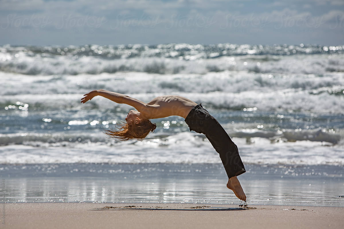 A redheaded boy back-flipping on a beach