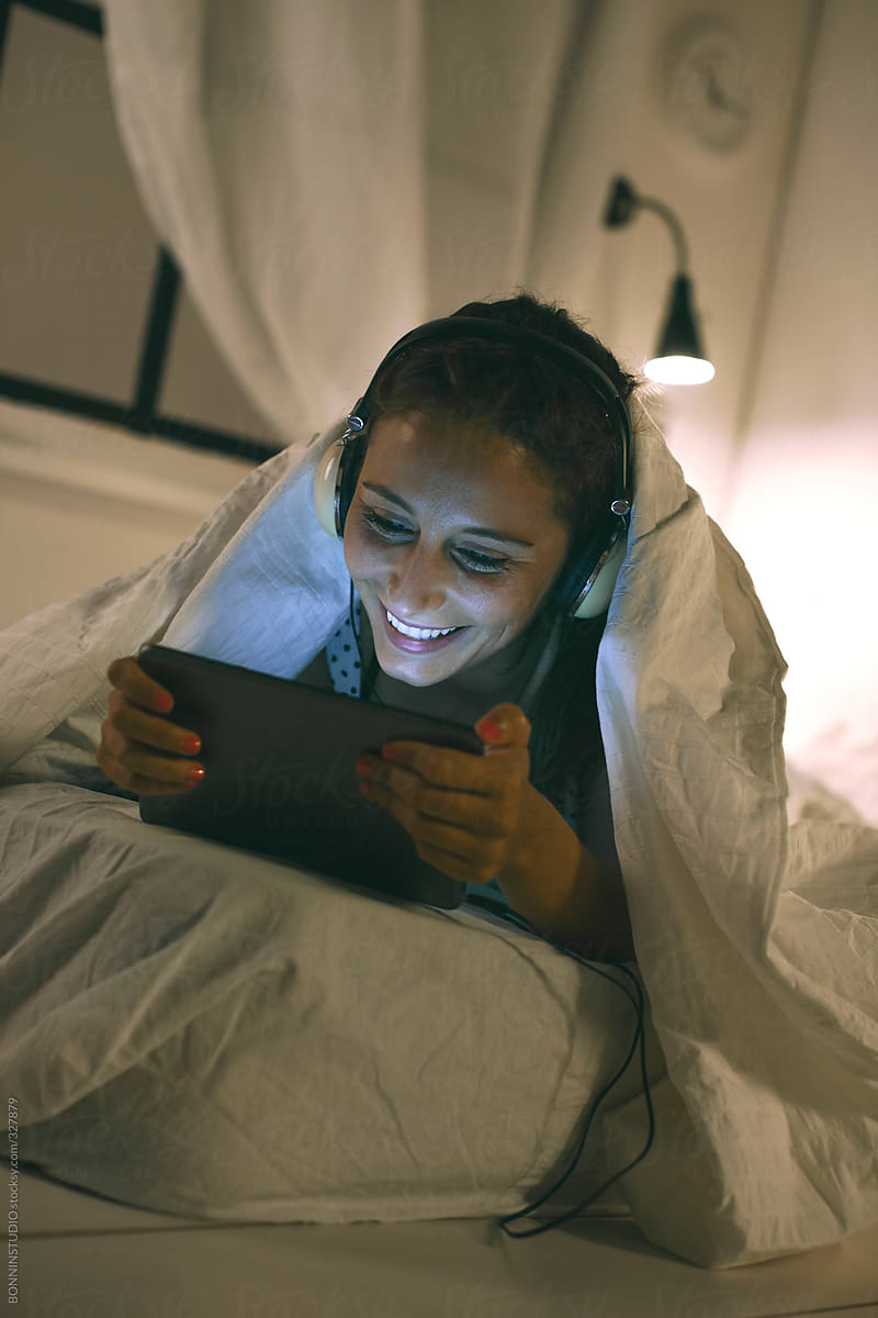 Woman Looking At Tv Shows With Digital Tablet Under A Cozy Bed Sheets