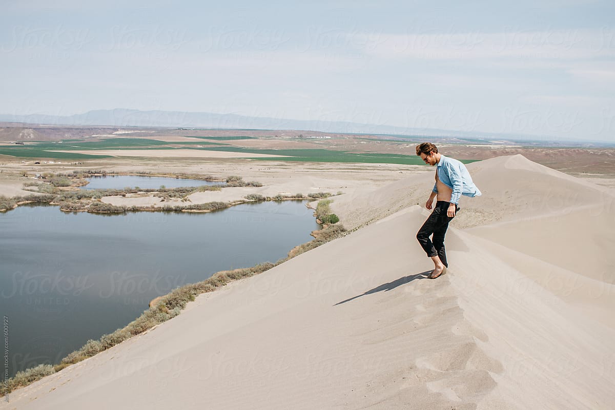 Young Man Walks Through Desert Hills With Shirt Un Buttoned And Open