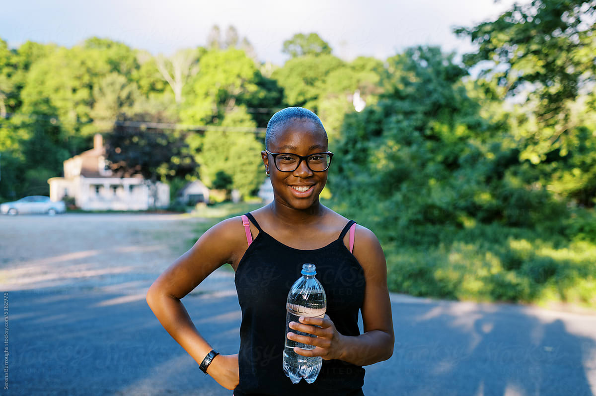 smiling fit black tween girl standing outdoors drinking water