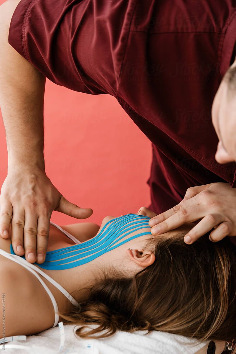 Masseur applying blue kinesio tapes on neck and face.