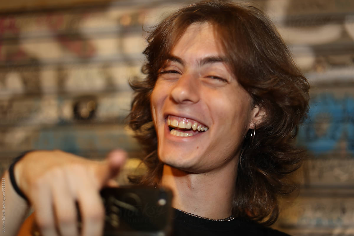 Young rock-style man laughing and pointing at the camera with phone