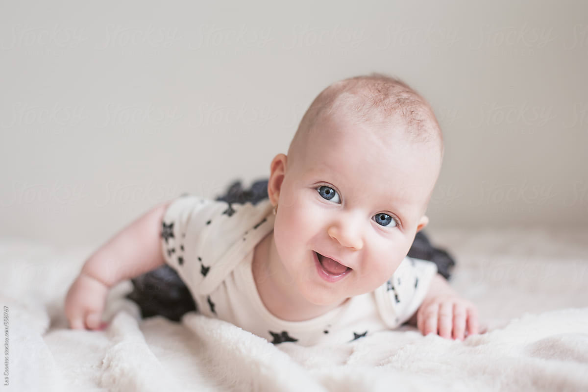 Adorable smiling baby lying on a bed and looking up curiously.