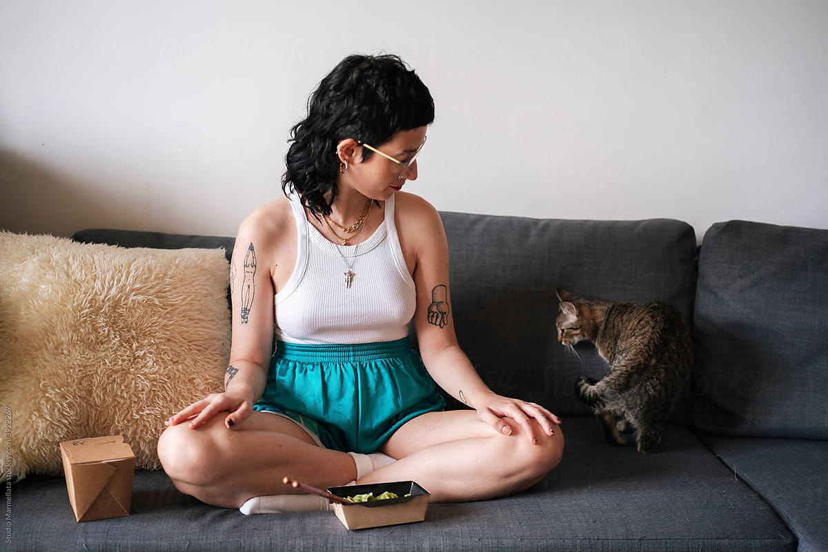 Content woman with food sitting on sofa near cat
