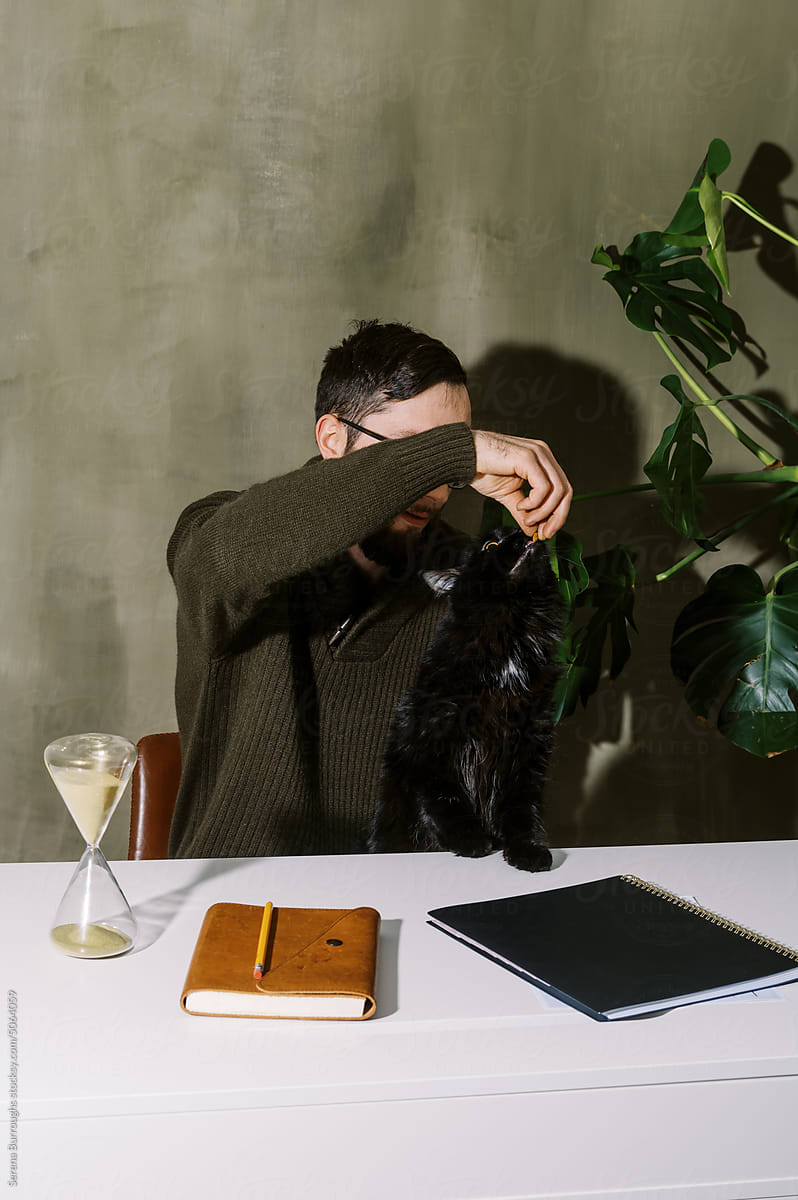 Man in his home office playing with his black cat