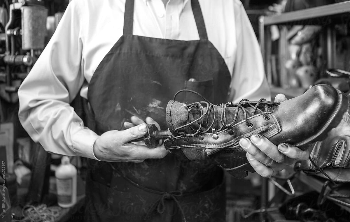 Black and white photo of a cobbler stretching a leather shoe with a hand stretcher